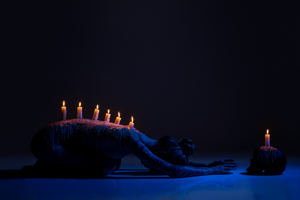 Burning candles on back of lady bowing down in darkness od Andrey Guryanov